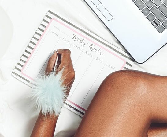 woman writing her weekly plan next to computer